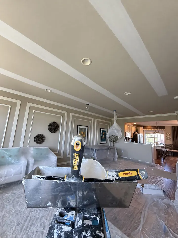 Wide view of repaired ceiling seams in a living and dining room with furniture and floors covered in protective plastic.