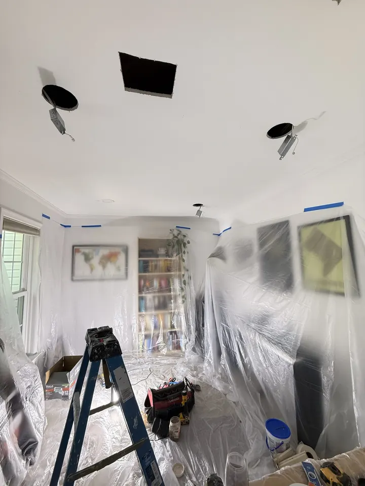 Ceiling with several openings cut for recessed light fixtures, with the room's furniture covered.