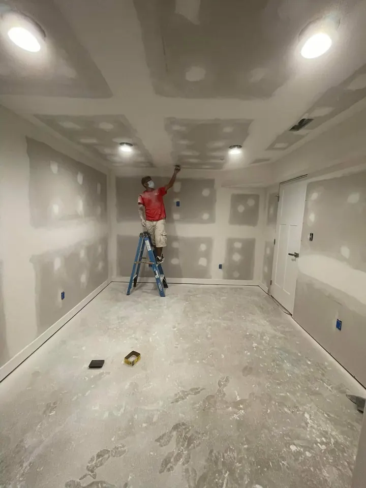 Installer sanding the ceiling in the same basement room after drywall boards, tape, and joint compound were applied.