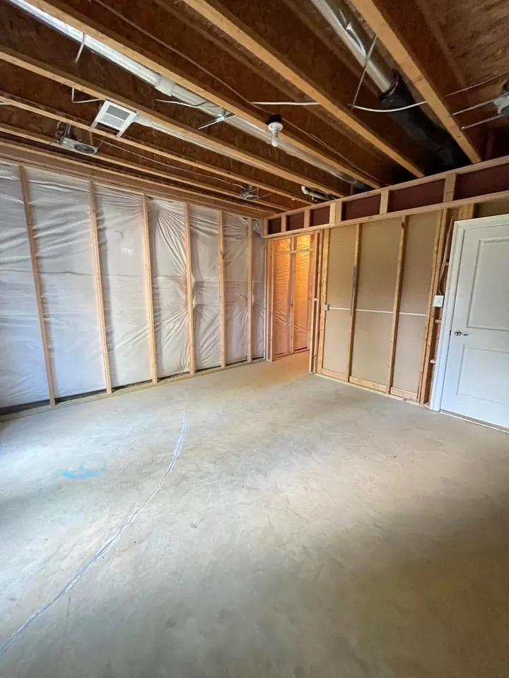 Basement room before drywall, with exposed wood wall framing, insulation, and an exposed structural beam overhead.