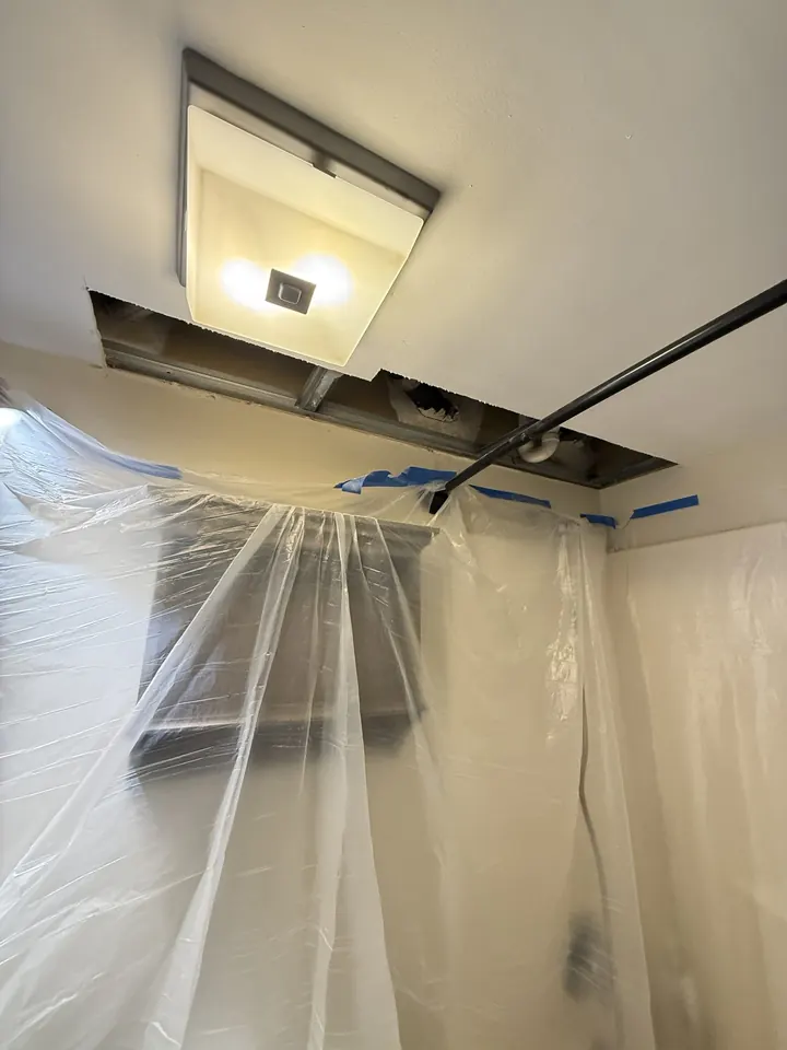 An access cut opened in a ceiling beside an existing light fixture.