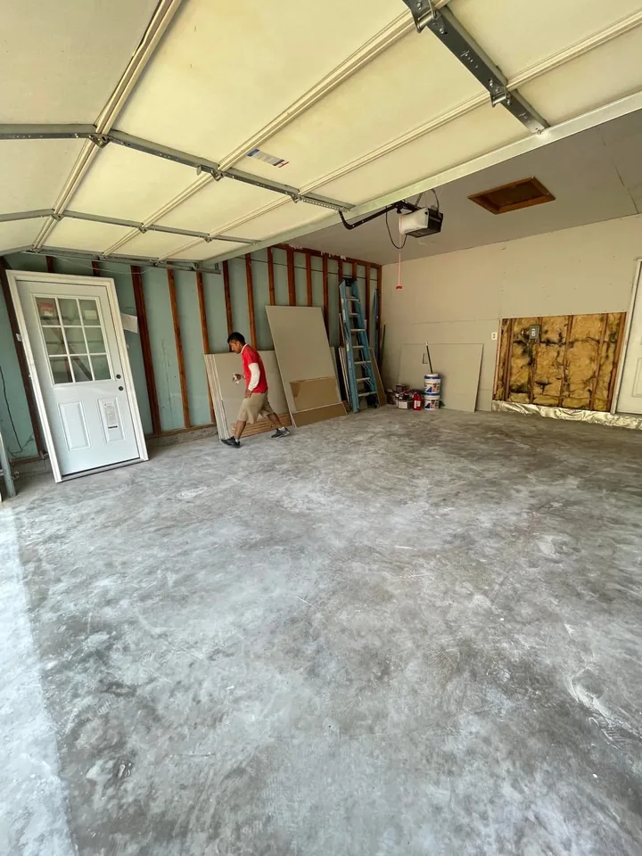 Garage before the work, with the wall framing and insulation exposed and drywall sheets on site ready to hang.