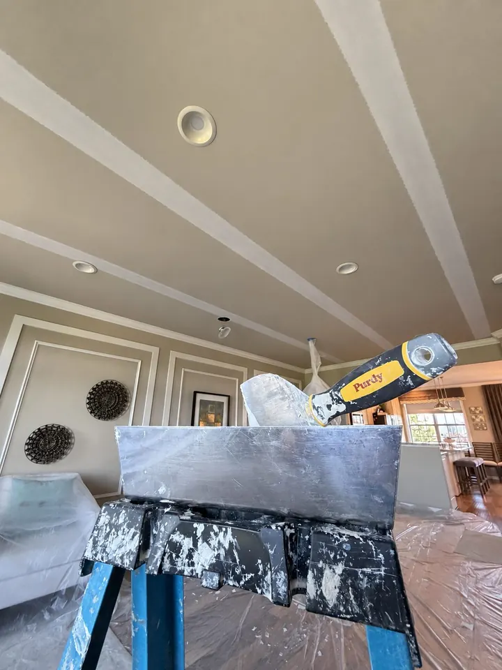 Close view of repaired and primed ceiling seams with a taping knife and mud pan in the foreground.